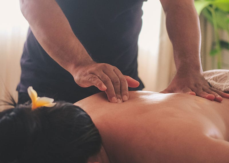 Traditional Balinese healer performing bodywork therapy on a client in a serene, natural setting, surrounded by tropical greenery and calming ambiance